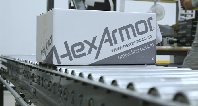 A HexArmor-branded box on a rolling conveyor belt in a HexArmor warehouse.