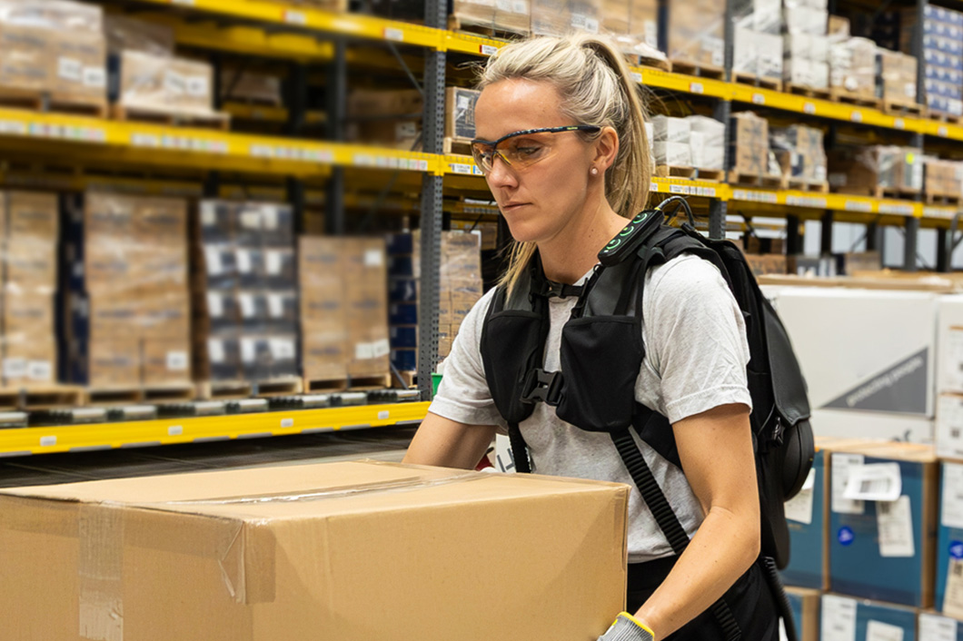 A worker using the SafeLift™ exosuit while lifting a box in a warehouse.
