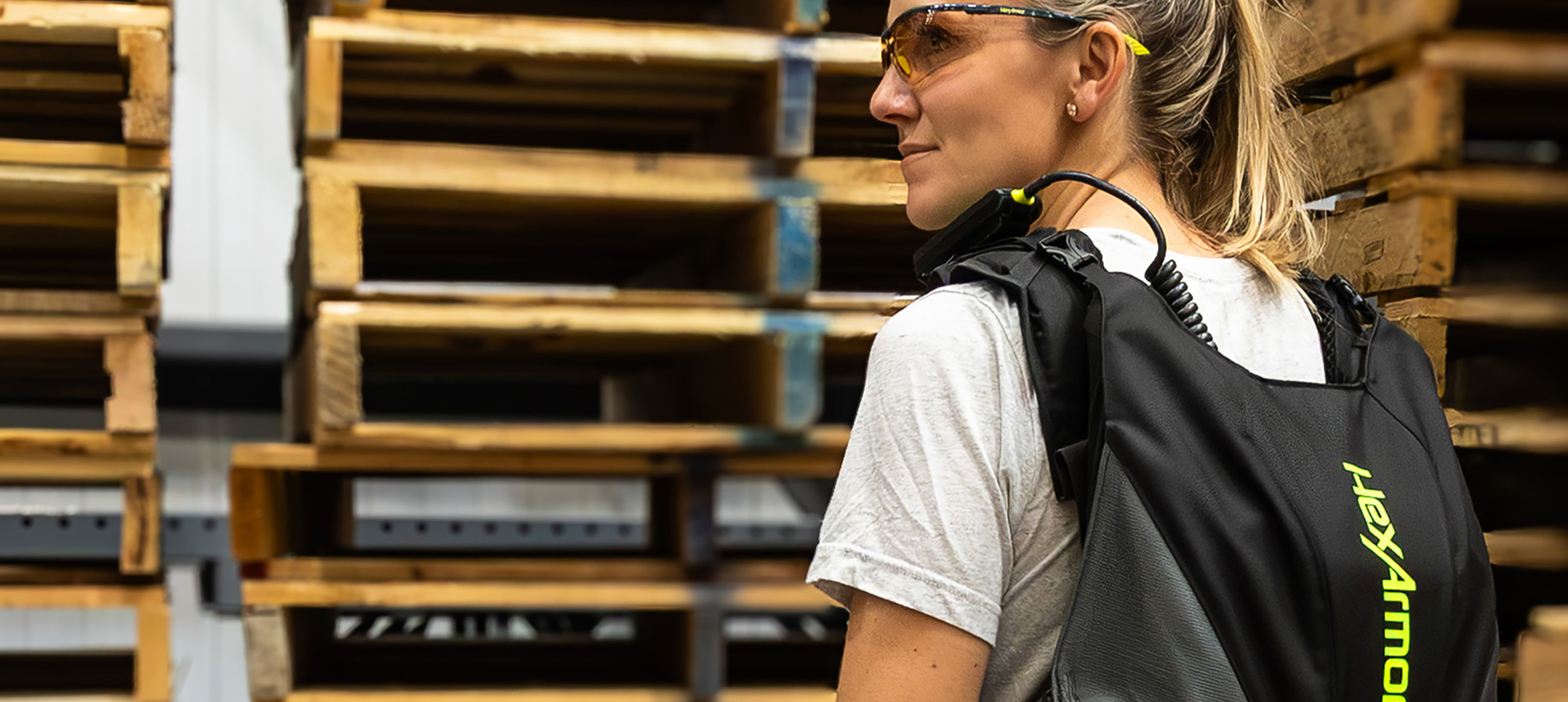Warehouse worker wearing the SafeLift™ exosuit among stacked pallets.