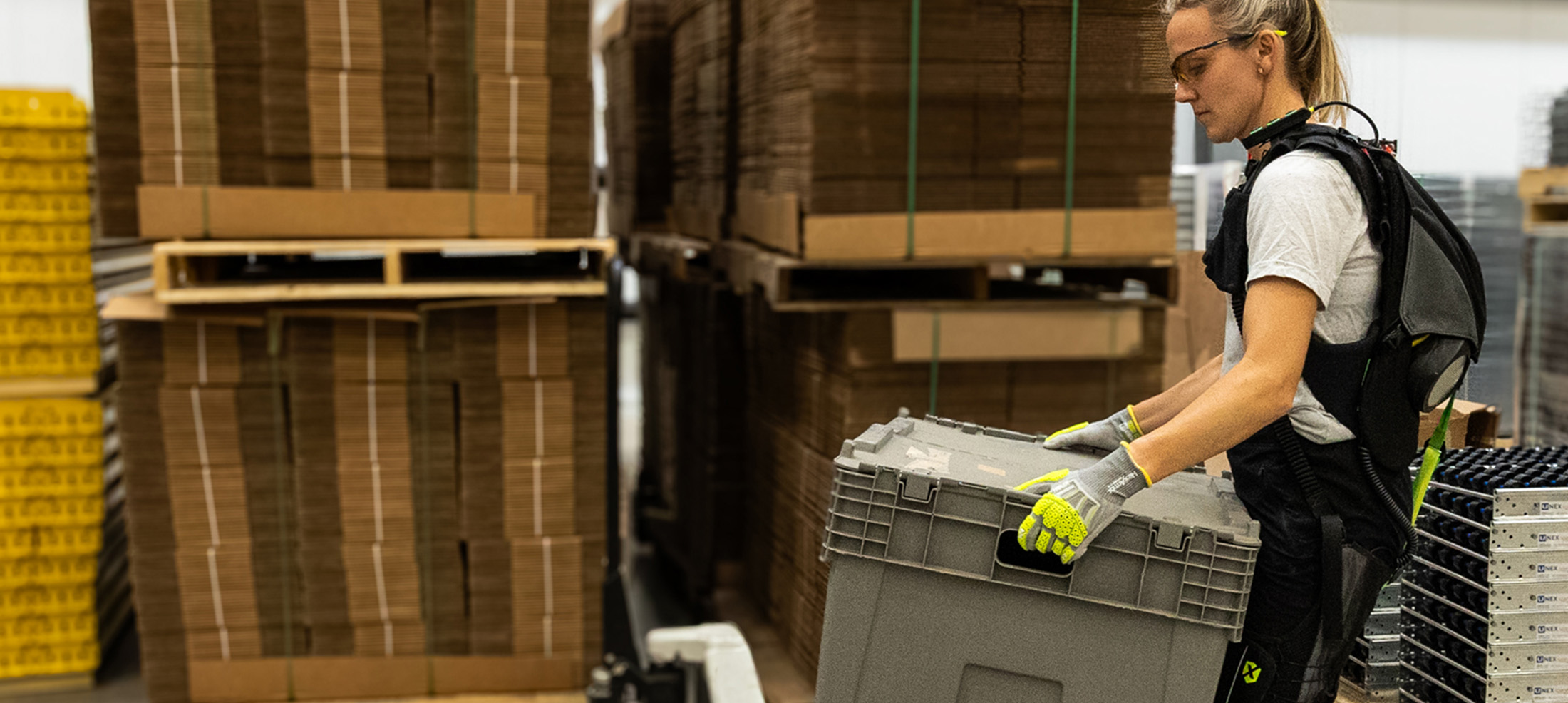 Worker lifting a tote while wearing the SafeLift™ exosuit in a warehouse.
